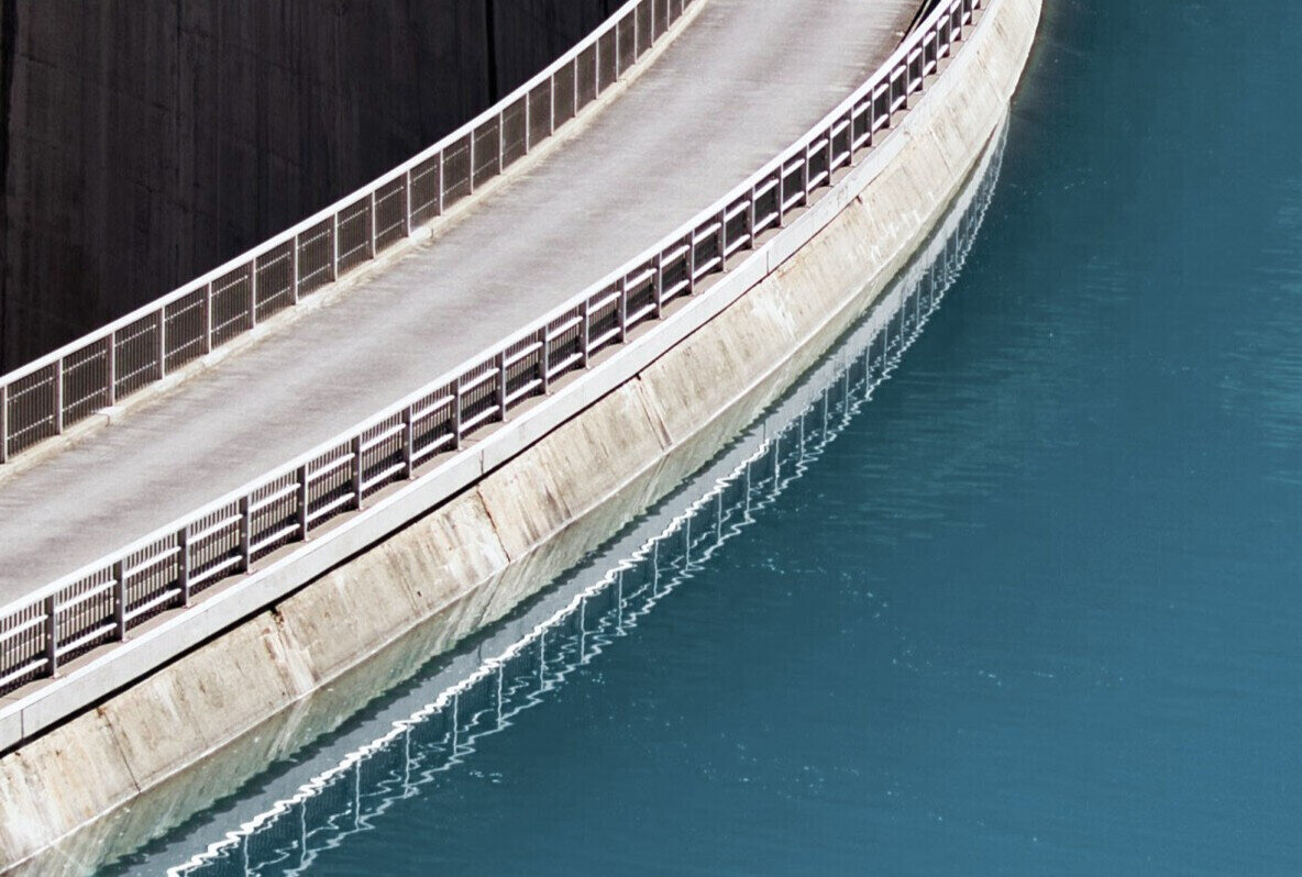 Detail der geschwungenen Staumauerkrone über dem türkisen Stausee